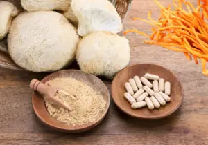 Wood slab with lion's mane mushrooms and cordyceps mushrooms next o powder and pill form versions of them.