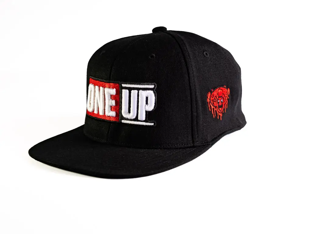 A black wool snapback baseball cap with embroidered One Up block stamp logo and red mushroom smiley face.