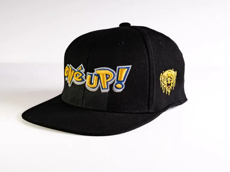 A black wool snap back baseball cap with embroidered Anime style gold One Up Logo and mushroom smiley face.