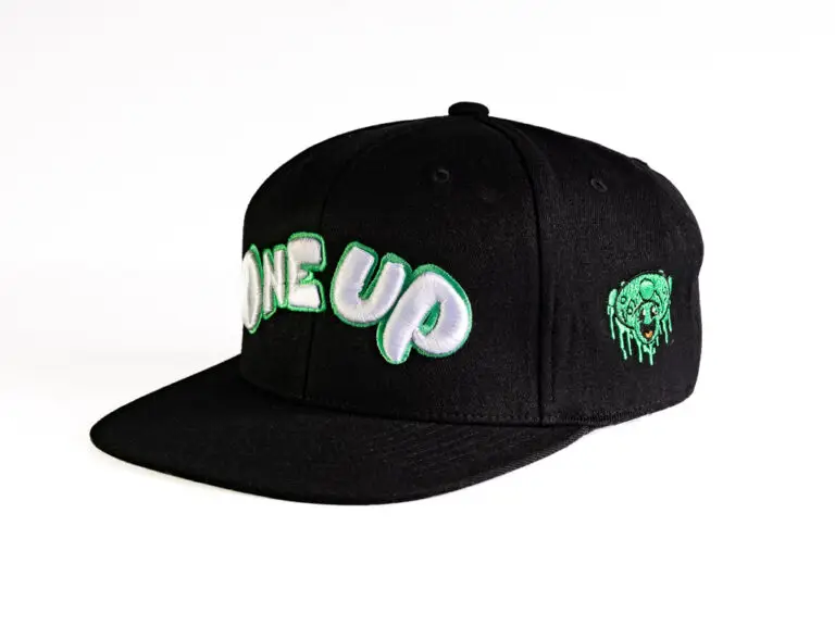 Black snapback ball cap with an embroidered green and white one up logo on the front , and a green mushroom smiley face on the side.